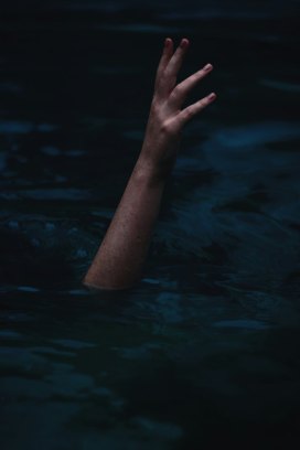 A human arm reaches upward through dark water.