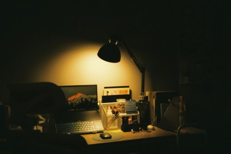A dimly lit writing desk, chair, computer, and lamp.